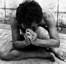 Skinny man praying naked on the sidewalk