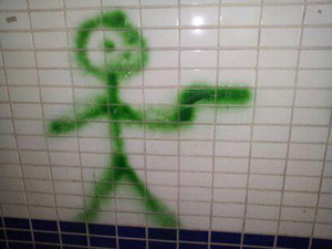 Stick figure with a gun spray painted on a bathroom wall in green