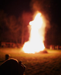 Guy sitting at a distance from a raging bonfire and smoke