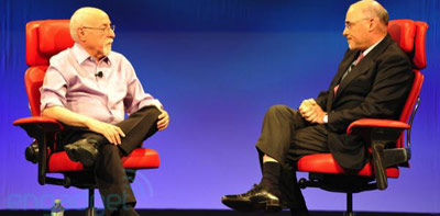 Two rich white CEO men sit on stage at a conference