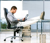 Man leaning back in a chair using his laptop at his desk