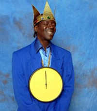Flava Flav in front of a blue backdrop wearing a clock