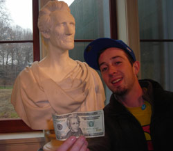 Lil Bot holds a 20 dollar bill up to a statue
