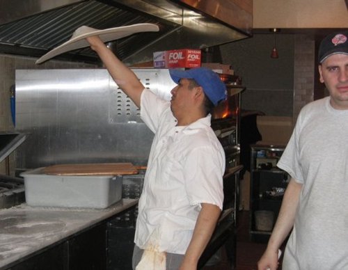 Two guys making pizza in the back of a restaurant