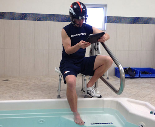 Peyton Manning putting his foot in a pool with helmet on