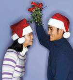 Guy holding mistletoe branch over a girl in a Santa hat