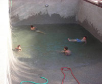 Empty backyard pool with boys playing in a puddle