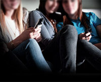 Three girls texting next to each other on Blackberry cell phones