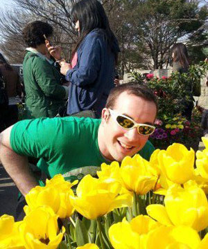 Casey smelling yellow flowers in a green tshirt