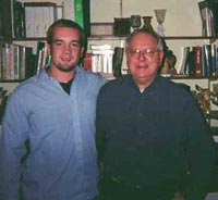 KC and a priest in front of a bookshelf
