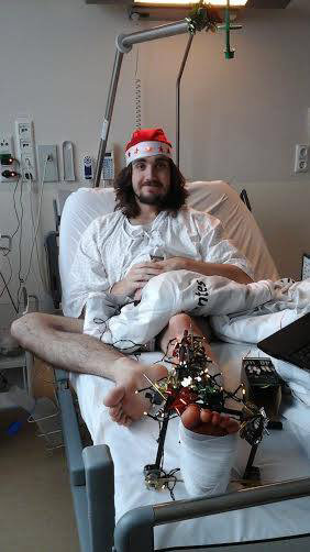 Cole laying in a hospital bed with a broken leg and Santa hat on