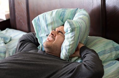 Man holding a pillow over his ears because of loud, annoying neighbor