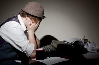 Man with hands on his face at a typewriter