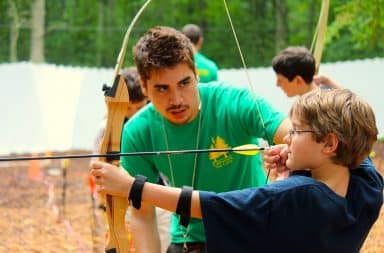 Boy shooting an arrow in the woods at camp