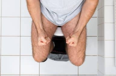 Man on toilet clenching his fists straining to poop