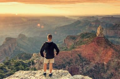 Man standing on edge of Grand Canyon at sunset looking out