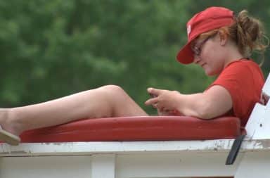 Female lifeguard on phone while on the chair at a pool