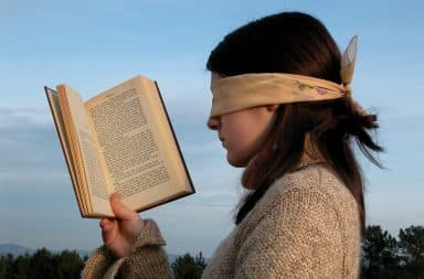 Woman holding book while wearing blindfold