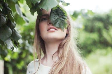 Woman rubbing her face on leaves of a tree for a beauty routine