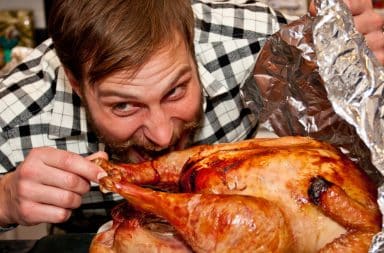 Man biting a whole turkey at Thanksgiving dinner table