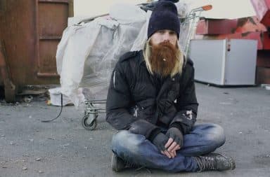 Drunk homeless man sitting next to a pile of garbage