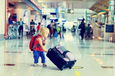 Toddler girl in airport alone carrying suitcase