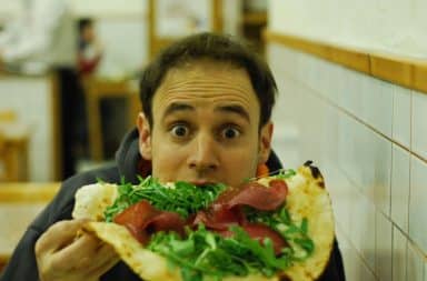 Man eating pizza with guilty look on his face