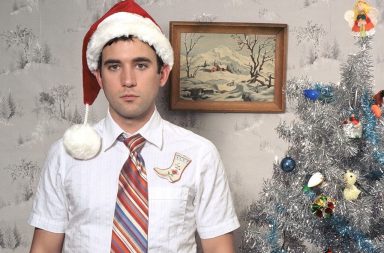 Man standing awkwardly in front of a Christmas tree