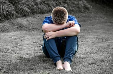 Sad boy with arms folded sitting outside on the grass