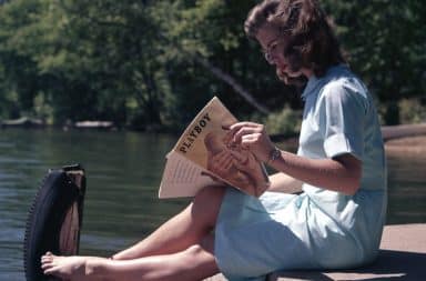 Woman reading Playboy magazine on a boat dock