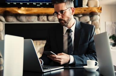 CEO man holding a phone in an office while on a laptop