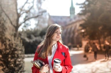 Woman on campus at small liberal arts college holding coffee and textbooks