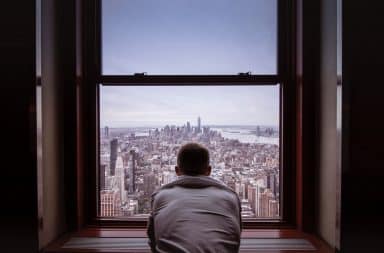 Man looking outside his apartment window at New York City