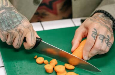 Gang member with tattoos on hands cutting carrots with a knife