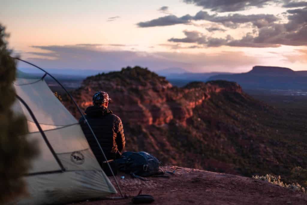 Man outside tent at night on a cliff edge